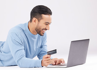 Image showing Laptop, credit card and happy asian man on studio floor for ecommerce, sale or cashback on grey background. Online shopping, deal and Japanese male customer smile for loan, payment or sign up promo