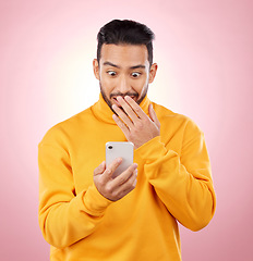 Image showing Phone, wow or gossip with a surprised man in studio on pink background reading fake news announcement online. Mobile, shock and wtf with a young male person on a social media website or the internet