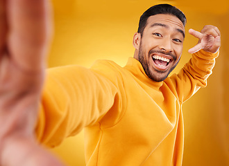 Image showing Peace sign, selfie and happy portrait of a man in studio with a hand, emoji and a smile. Male asian fashion model excited on a yellow background with a positive icon for social media profile picture