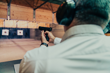 Image showing A man practices shooting a pistol in a shooting range while wearing protective headphones