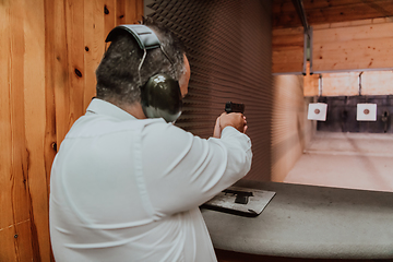 Image showing A man practices shooting a pistol in a shooting range while wearing protective headphones