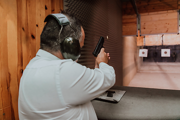 Image showing A man practices shooting a pistol in a shooting range while wearing protective headphones