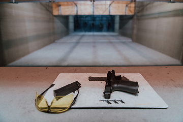 Image showing Shooting equipment in front of the target. Pistol, goggles and headphones on the table of a modern shooting range