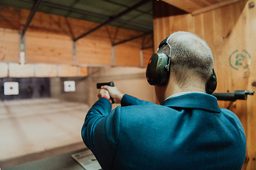 Image showing A man practices shooting a pistol in a shooting range while wearing protective headphones