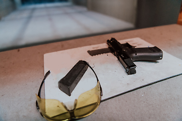 Image showing Shooting equipment in front of the target. Pistol, goggles and headphones on the table of a modern shooting range