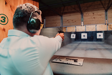 Image showing A man practices shooting a pistol in a shooting range while wearing protective headphones