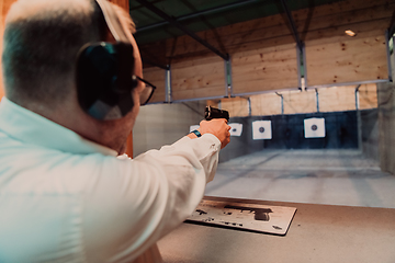 Image showing A man practices shooting a pistol in a shooting range while wearing protective headphones