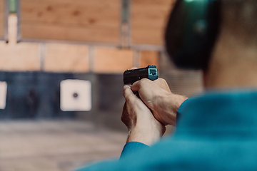 Image showing A man practices shooting a pistol in a shooting range while wearing protective headphones