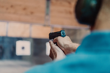 Image showing A man practices shooting a pistol in a shooting range while wearing protective headphones