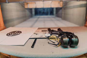 Image showing Shooting equipment in front of the target. Pistol, goggles and headphones on the table of a modern shooting range