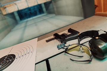 Image showing Shooting equipment in front of the target. Pistol, goggles and headphones on the table of a modern shooting range