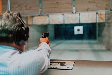 Image showing A man practices shooting a pistol in a shooting range while wearing protective headphones