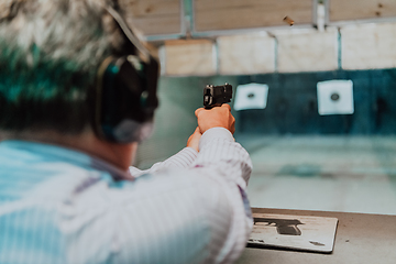 Image showing A man practices shooting a pistol in a shooting range while wearing protective headphones