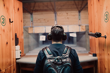 Image showing A man practices shooting a pistol in a shooting range while wearing protective headphones