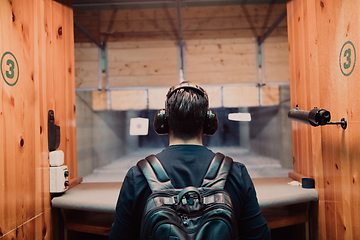 Image showing A man practices shooting a pistol in a shooting range while wearing protective headphones