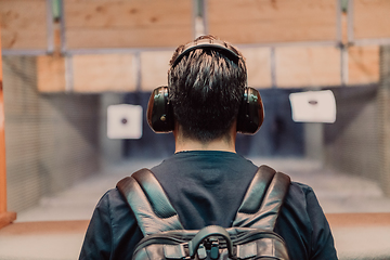 Image showing A man practices shooting a pistol in a shooting range while wearing protective headphones