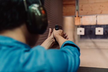 Image showing A man practices shooting a pistol in a shooting range while wearing protective headphones