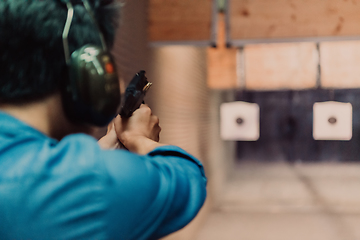 Image showing A man practices shooting a pistol in a shooting range while wearing protective headphones
