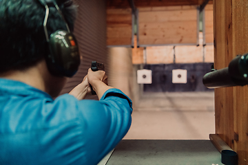 Image showing A man practices shooting a pistol in a shooting range while wearing protective headphones