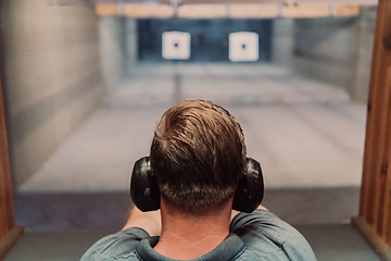 Image showing A man practices shooting a pistol in a shooting range while wearing protective headphones