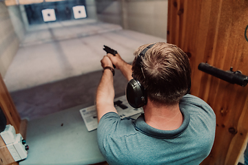 Image showing A man practices shooting a pistol in a shooting range while wearing protective headphones