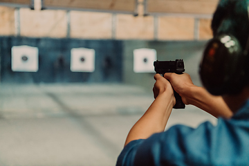 Image showing A man practices shooting a pistol in a shooting range while wearing protective headphones