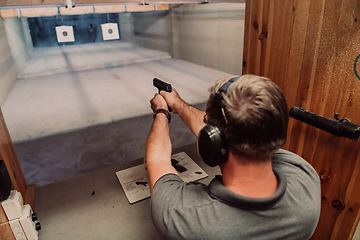 Image showing A man practices shooting a pistol in a shooting range while wearing protective headphones