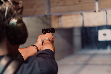 Image showing A man practices shooting a pistol in a shooting range while wearing protective headphones