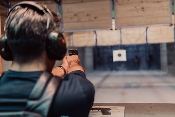 Image showing A man practices shooting a pistol in a shooting range while wearing protective headphones