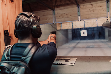 Image showing A man practices shooting a pistol in a shooting range while wearing protective headphones