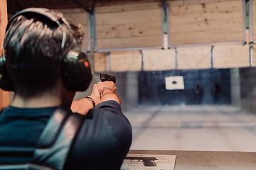 Image showing A man practices shooting a pistol in a shooting range while wearing protective headphones