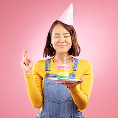 Image showing Birthday cake candle, wish and Asian woman with fingers crossed, hope and celebrate party, present or studio gift. Praying, emoji icon sign and person with dessert, candy or sweets on pink background