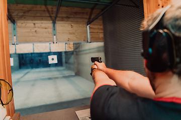 Image showing A man practices shooting a pistol in a shooting range while wearing protective headphones