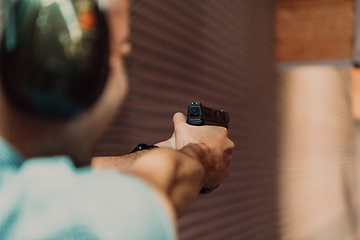 Image showing A man practices shooting a pistol in a shooting range while wearing protective headphones