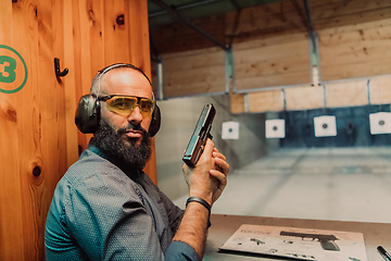 Image showing A man practices shooting a pistol in a shooting range while wearing protective headphones