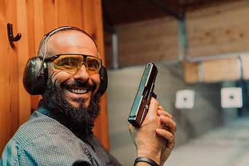 Image showing A man practices shooting a pistol in a shooting range while wearing protective headphones