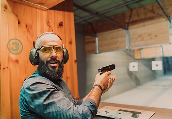 Image showing A man practices shooting a pistol in a shooting range while wearing protective headphones