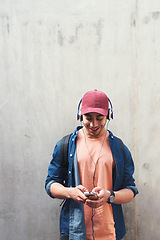 Image showing Happy, headphones and man with phone on a wall for social media, communication or a chat. Smile, technology and a male college student streaming or listening to a podcast on a mobile app with mockup