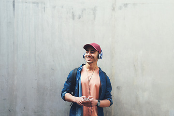 Image showing Man, listening and music with smile in outdoor with concrete wall background for entertainment. Happy, face and guy with headphones is excited with tech for streaming radio with student for sound.