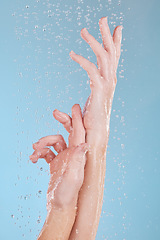 Image showing Water drops, skin and person washing hands in studio on blue background for hygiene or hydration. Cleaning, wellness and skincare with a woman in the bathroom for sustainability or to remove bacteria