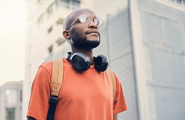 Image showing .Black man, student and walking outdoor on a city street while thinking of music and freedom. A serious African person with a backpack on an urban road with casual style and fashion for travel.