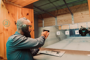 Image showing A man practices shooting a pistol in a shooting range while wearing protective headphones