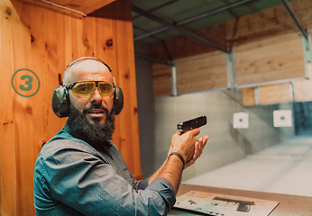 Image showing A man practices shooting a pistol in a shooting range while wearing protective headphones