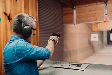 Image showing A man practices shooting a pistol in a shooting range while wearing protective headphones