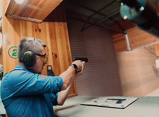 Image showing A man practices shooting a pistol in a shooting range while wearing protective headphones