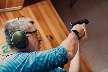 Image showing A man practices shooting a pistol in a shooting range while wearing protective headphones