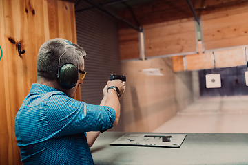 Image showing A man practices shooting a pistol in a shooting range while wearing protective headphones