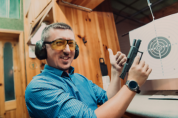 Image showing A man practices shooting a pistol in a shooting range while wearing protective headphones