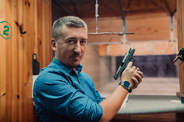 Image showing A man practices shooting a pistol in a shooting range while wearing protective headphones