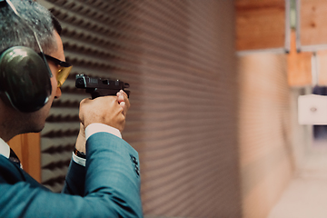 Image showing A man practices shooting a pistol in a shooting range while wearing protective headphones